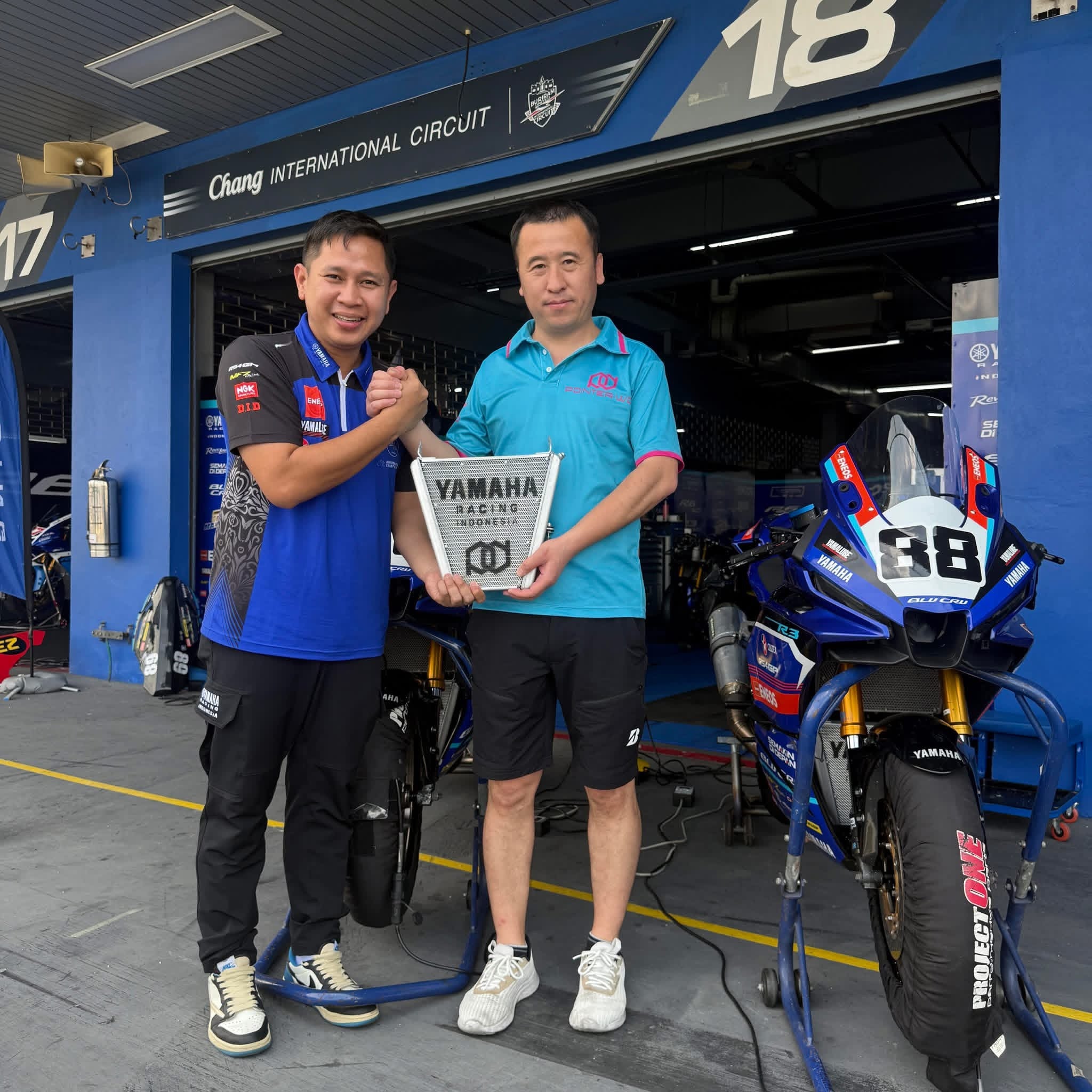 Two men standing in front of a Yamaha motorcycle in a garage with 'Chang International Circuit' branding.